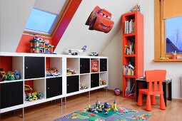 Moderne Regalschränke, halbhoch, mit schwarzen Modulen, Stuhl und Hochregal in Rot im Kinderzimmer unter dem Dach