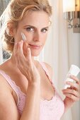 A blonde woman applying face cream