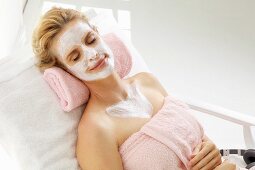 A blonde woman relaxing with a nourishing mask on her face and chest