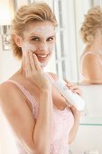 A blonde woman in front of mirror applying cleansing milk to her face