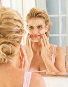 A blonde woman in front of a mirror applying cleansing milk to her face