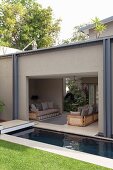 View into roofed seating area with sofas behind lawn and pool