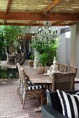 Wooden table and crystal chandelier on roofed terrace given the impression of space by mirrored wall