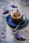 A chocolate cupcake with coffee buttercream and lavender flowers on a blue plate