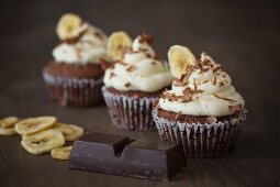 Chocolate cupcakes with a banana topping with cooking chocolate and banana chips next to it