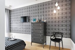 Dark grey chest of drawers and black chair against grey and black tartan wallpaper in bedroom