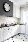 Antique station clock on black extractor hood housing in white, elegant, country-style fitted kitchen