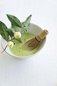 Matcha tea with a bamboo whisk in a tea bowl on a white surface