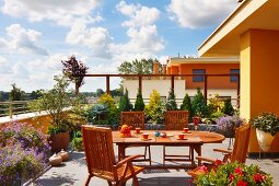 Teak oval table and chairs on sunny, planted roof terrace in contemporary housing complex