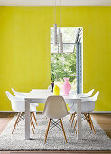 White classic chairs around modern dining table on Berber rug in front of wall painted in bright lemon yellow