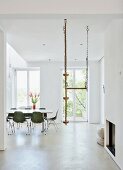 Green shell chairs and climbing rope hanging from ceiling in minimalist, white dining room