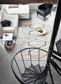 View down black industrial spiral staircase to sofa, large dish on floor used as coffee table and geometric rug