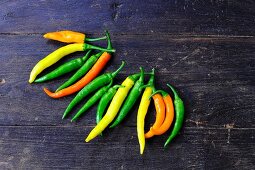 Various different coloured chilli peppers on a wooden surface