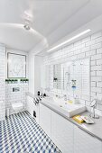 Modernes Bad in Weiß mit Wand- & Bodenfliesen, langgestrecktem Waschtisch mit Unterschränken & Lichtleiste über Spiegel, im Hintergrund modernes Wandbild über Hängetoilette