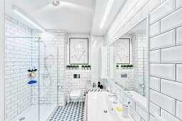 Modernes Bad in Weiß mit Wand- & Bodenfliesen, Lichtleisten über Waschtisch & verglaster bodenebener Dusche, im Hintergrund modernes Wandbild über Hängetoilette