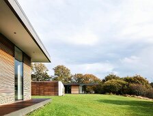 Wohnhaus der Klassischen Moderne mit Holz- Glasfassade und auskragendem Dach in sommerlichem Landschaftsgarten