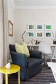 Dark grey armchair & yellow side table in front of work area with white desk & swivel chair