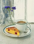 A slice of almond tart with raspberries served with a cup of coffee