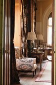 Armchair upholstered with Uzbek pattern in wood-clad window niche with floor-length curtains and antique side tables in background