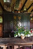 Blumenstrauss auf rustikalem Holztisch vor Vintage-Vitrinenschrank in Landhausküche