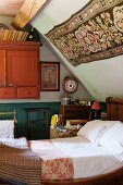 Antique sleigh bed under sloping bedroom ceiling with floral wall hanging