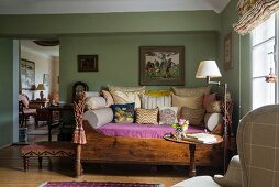 Antique daybed with wooden frame, many scatter cushions in traditional living room with green-painted walls