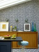 Black counter, fifties-style pale-wood sideboard and wallpaper with retro pattern