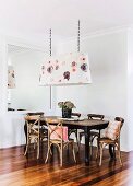 Bentwood chairs with crossed backrests around dining table below floral pendant lamp next to large mirror on wall