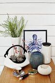 Sukkulenten in weisser, korbähnlicher Porzellanschale, verschiedene Vasen und Bild mit Tintenfischmotiv vor weisser Holzwand