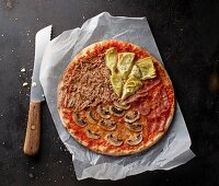 A tuna, mushroom, Parma ham and artichoke pizza on a piece of paper with a knife