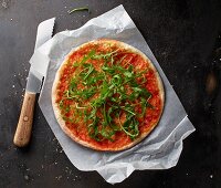 Pizza Margherita with rocket on a piece of paper with a knife