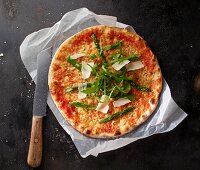 Pizza Margherita with asparagus, rocket and grated Parmesan on a piece of paper with a knife