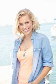 Blonde Frau mit apricot Top und Jeanshemd am Meer