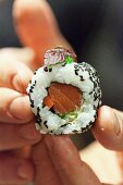 Hände halten ein Uramaki-Sushi mit Lachs