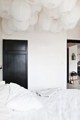 Double bed with white bed linen below a sea of paper lanterns on ceiling; black-painted interior door in background