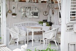 Blick auf Holztisch und weiße Rattanstühle in Shabby Gartenpavillon mit weiss lasierten Holzwänden