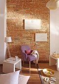 Fifties armchair with lilac cover and lamp on modern, white side table against brick wall