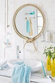 Round bathroom mirror with decorative rope frame in a white bathroom with wood-panelled walls