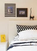 Mixture of black and white patterns on pillow covers, decorative picture frames and cat ornament on bed headboard