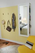 Praktische Haken auf hellgelber Wandfläche neben Spiegel mit verdecktem Stauraum im Schlafzimmer