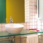 Washstand with white china basin on glass counter against white-tiled wall with red grouting