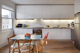 Simple wooden chairs and Tripp Trapp highchair around table in kitchen with fitted cabinets