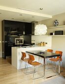 Designer-Hängeleuchte über Tisch und Schalenstühle mit Retro Flair, daneben monolithische Theke in Weiß in offener Küche