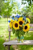 Sommerstrauss aus Sonnenblumen & blauem Rittersporn auf Bank im Freien