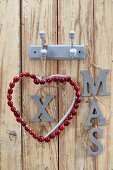 Weihnachtliche Wanddekoration mit Herz aus Cranberries & Schriftzug XMAS aufgehängt an Garderobenhaken