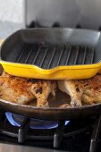 Chicken hearts being fried in a pan weighed down with another pan