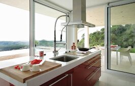 View from red kitchen counter through glass walls onto partially roofed terrace