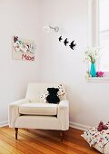 Soft toy sitting on elegant, white armchair in corner of child's bedroom below pinboard and bird ornaments on wall