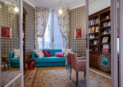 Light blue couch in front of window with draped curtains and patterned wallpaper in eclectic interior seen through open double doors