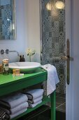 Green-painted washstand with countertop sink next to shower area with black and white patterned wall tiles